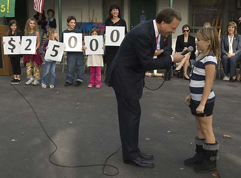 Colfax Avenue Charter Elementary School Foundation Chairman Lowell Milken asks a young Colfax Avenue Elementary student named Kayley to tell him the amount displayed on the cards, which is the total amount of the Milken Educator Award to be presented to one of the school's outstanding teachers.