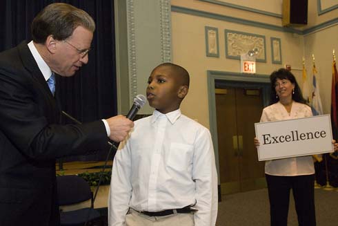 John J. Pershing West Magnet School Milken Family Foundation Chairman Lowell Milken asks a young Pershing student to define the meaning of the word that Foundation Trustee Joni Milken-Noah is holding in her hands.